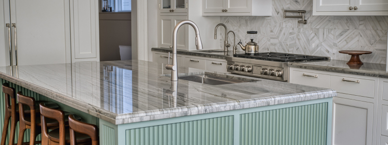 Modern kitchen with marble island and Jema Single-Handle Pull-Down Kitchen Faucet, featuring white cabinetry, stainless appliances, and warm wood seating accents.