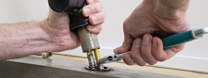 Close-up of hands installing a kitchen faucet beneath countertop, using plumbing tools to secure fittings during a kitchen sink fixture replacement project.