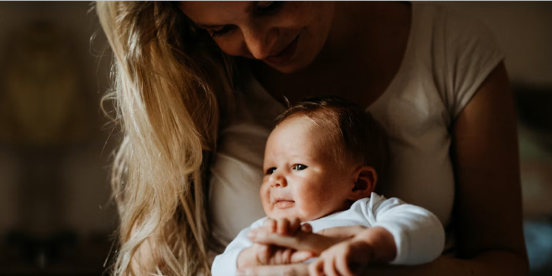 Parent cradles a smiling baby in warm natural light, capturing a tender family moment that conveys comfort, care, connection, and love at home.