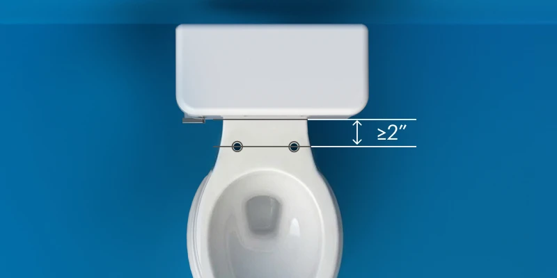 Overhead diagram of a toilet showing a minimum clearance of 2 inches between the mounting bolt holes and toilet tank for proper bidet seat installation.