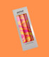 Three neon hand marbled candles in pink, orange, and yellow, in a foiled gift box.