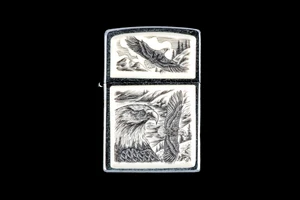 This is a unique originally hand etched Eco-Ivory Scrimshaw Eagle Face with Soaring Eagle designed Zippo Lighter! The top of the flip lighter has a a Soaring Eagle Top piece.  The Zippo is a Brushed Chrome finish. Each lighter has a bottom stamp signifying the year it was made, is refillable. All windproof lighters are American made in Bradford, PA factory and come packaged in a gift box.  This is part of the Save the Elephant Collection and was originally hand etched by Linda Layden. The SKU is NC 54 - 142

The Zippo Lighter is 2.24" x 1.51" x 0.59".  It weighs 2.04 oz.
