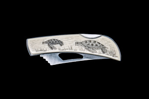 This beautiful originally hand etched Turtle design on a Stainless Steel Silver Hawk Knife.  The back of the knife has a belt clip and all the knifes come with the pictured sheath.  It is a lock blade knife and a useful pocket knife. The artwork was originally hand etched by Linda Layden.  The dimensions of the Silver Hawk knife with the blade closed are 3.00" x 0.96" x 0.55".  The blade itself is approximately 2.35" making the width of the knife with an open blade 5.35".  The SKU is NC 14 - 405.

Linda Layden has been making beautiful works of art in the scrimshaw field for over 40 years.  Originally a hobby that became a full time job.  Her work can be found in gift shops, galleries and museums across the world.