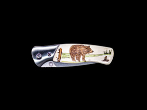 This absolutely stunning hand etched Colored Brown Bear design on a Buck 835 Folding Selkirk Pocket Knife with a bovine bone front handle.  The back of the knife has a belt clip/ money clip.  It is a lock blade knife and a useful pocket knife.  The artwork was originally hand etched by Chris Tyson.  The knife is a liner lock blade, meaning it was made for one handed opening.  The dimensions of the Buck 835 Folding Selkirk Pocket Knife with the blade closed are 4.29" x 1.23" x 0.60".  The blade itself is approximately 3.25" making the width of the knife with an open blade 7.5".  The SKU is NC 835 - 102C.

The stunning design that was hand etched is of a brown bear!

The artwork was originally hand etched by Chris Tyson. A very versatile artist from New England!

The scrimshaw is inked with a colored india ink and sealed with renaissance wax, which is used by museums for antique restoration.  It also helps bring out the beauty of the artwork as well as in the cow bone. The knife is water resistant, but not waterproof.

Buck 420HS Steel.  This is Buck's standard blade material because it approaches the wear resistance of high carbon alloys while delivering the corrosion resistance of chromium steels.  Add in Buck's exclusive heat-treat process for durability and corrosion resistance.

Drop Point Blade, is full bellied with a strong thick point for heavier tasks.  The drop point blade is strong and versatile.