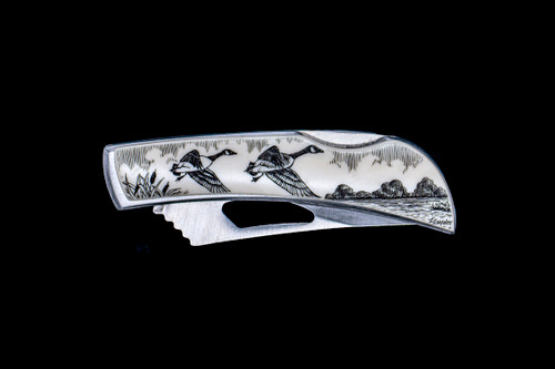 This beautiful originally hand etched Canadian Geese design on a Stainless Steel Silver Hawk Knife.  The back of the knife has a belt clip and all the knifes come with the pictured sheath.  It is a lock blade knife and a useful pocket knife. The artwork was originally hand etched by Linda Layden.  The dimensions of the Silver Hawk knife with the blade closed are 3.00" x 0.96" x 0.55".  The blade itself is approximately 2.35" making the width of the knife with an open blade 5.35".  The SKU is NC 14 - 108.

Linda Layden has been making beautiful works of art in the scrimshaw field for over 40 years.  Originally a hobby that became a full time job.  Her work can be found in gift shops, galleries and museums across the world.