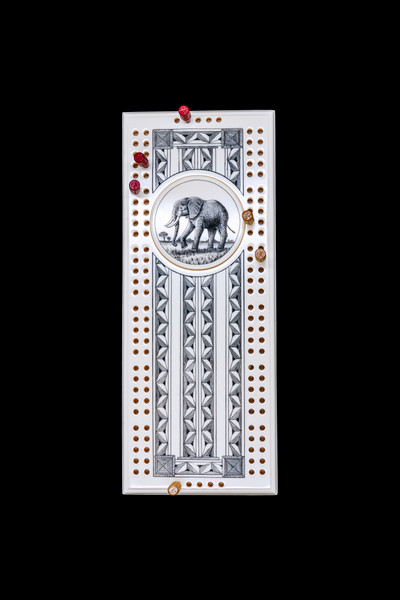 Elephant Cribbage Board with pegs.  This wonderful two person and our two team cribbage boards is a beautiful accent piece for your home or take it on the road for use as a travel cribbage board.  With the magnet holding the center piece and pegs in place it is a stunning travel cribbage board. 

This is a beautiful originally hand etched Elephant Design Eco - Ivory Scrimshaw Cribbage Board!  The center circular piece has a magnet holding it in place.  Pushing on the base of the piece pops the Large round off the board, where the pegs are stored.  All cribbage boards come with 3 red and 3 white/yellow wooden pegs. 

The cribbage board itself is made for two players or teams.  The board has a native geometric design that was originally hand etched.  The large round piece has a magnet on the back to keep it secured to the board and store the pegs.  The pegs are made of wood.  This is part of the Save the Elephant Collection and was originally hand etched by Linda Layden.  The SKU is NC 53 - 138.