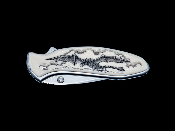 NC 1600 500 Soaring Dragon.  This stunning originally hand etched Dragon design on a Kershaw 1600 Chive Speedsafe Assisted Opening Pocket Knife.  The back of the knife has a belt clip/ money clip and the knifes come with the pictured sheath.  It is a lock blade knife and a useful pocket knife.  The artwork was originally hand etched by Linda Layden.  The dimensions of the Kershaw 1600 Chive Pocket knife with the blade closed are 2.95" x 0.92" x 0.53".  The blade itself is approximately 1.9" making the width of the knife with an open blade 4.85".  The SKU is NC 1600 - 500.

This unique etching has a soaring Dragon!

Linda Layden has been making beautiful works of art in the scrimshaw field for over 40 years.  Originally a hobby that became a full time job.  Her work can be found in gift shops, galleries and museums across the world.  

It is a bead-blasted 1. 9” high-performance blade made of 420HC steel offers good edge retention and excellent corrosion resistance. With a matching stainless steel handle is resistant to corrosion and also finished with a non-reflective matte bead-blasted finish.  The acrylic resin is placed on top of the handle.  Handle features SpeedSafe assisted opening, secure frame lock, Tip-lock slider and convenient single-position pocket clip.  Capable of everyday cutting tasks at home or at work such as cutting zip-ties, stripping small wire, slicing fruit and removing staples.  Perfect for everyday carry in a pocket, purse, backpack, briefcase, on a belt or around the neck with the handle’s predrilled lanyard hole.