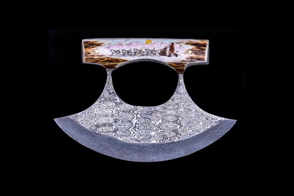 This beautiful etched Sleigh Dogs colored ink design on Shed Antler handle on a Damascus Ulu Blade.  

An ulu is an all-purpose knife traditionally used by Inuit, Iñupiat, Yupik, and Aleut women. The knife can be used in a variety of diverse ways such as skinning and cleaning animals, cutting a child's hair, cutting food, and sometimes even trimming blocks of snow and ice used to build an igloo.

The artwork was originally hand etched by Bill Feeney. He received a Bachelor of Arts degree in Mathematics from Saint Francis College in Bidderford, Maine, In 1973 I accepted a teaching position at Westport High School where I met Robert Rayno, the art teacher. As part of the class curriculum, he taught a section on scrimshaw. I sat in on many of his classes and purchased the necessary tools and ivory to begin etching. Combining my natural artistic ability with the techniques learned from Mr. Rayno, the cornerstone of "Spouting Whale" was established.

The weight of the knife is 8.99 ounces and the dimensions of the DM 005 Knife closed are 5.44" x 3.77" x 0.88".   The SKU is DM 005 242C.  The knife comes with the pictured leather sheath.

  During the winter season, moose shed their antlers before regrowing them in the spring. The shedding process, also known as casting, is a normal event that occurs annually for many male cervids—a group of hoofed mammals like moose, deer and elk.

Damascus steel is a type of steel easily recognisable by its wavy patterned design. Aside from its sleek look and beautiful aesthetics, Damascus steel is highly valued as it is hard and flexible while maintaining a sharp edge. Weapons forged from Damascus steel were far superior to those formed from just iron.  It a combination of carbon steel and regular steel that is folded 71 times.  

Features:
Shed Antler Handle
Scrimshaw
Etched
Sleigh Dogs

Eskimo

Ulu
Damascus Blade

Carbon and regular Steel
Folded 71 times