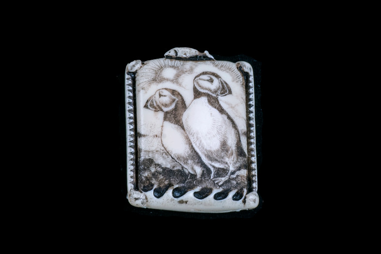 MPD PN 14 Puffin Zoom.  This is a beautiful originally hand etched Puffin designed pin/pendant. The backing of this piece has the findings to be a pin, as well as a pendant.  They come with an 18" Silver Plated Chain.  This is part of the incredible line of Mossup Valley Designs that we carry, with the wonderful artist Rachel Badeau.  The dimensions of the necklace are 1.21" x 1.57" x 0.35".  The SKU is MVD PN 14.

Rachel Badeau has been etching and engraving in a variety of media for over thirty years.  Her work, characterized by fine line and intricate detail, attempts to touch the hearts and emotions of others.  All while reflecting her love of animals, nature and the human spirit.  

The resin scrimshaw piece is originally hand etched by Rachel Badeau.  We make a mold of the original piece and do an open cast pour of our resin mixture.  The pieces are removed from the mold and sanded and inked.