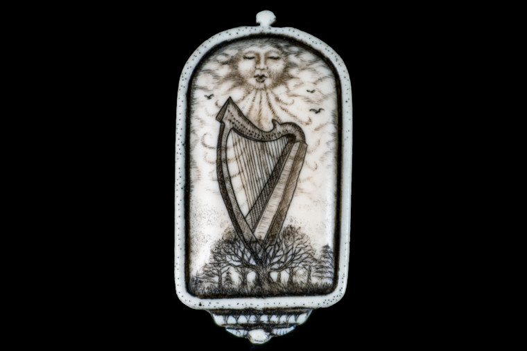 This distinct originally hand etched Wind Harp designed pin/pendant.  The backing of this piece has the findings to be a pin, as well as a pendant.  They come with an 18" Silver Plated Chain.  This is part of the incredible line of Mossup Valley Designs that we carry, with the wonderful artist Rachel Badeau.  The dimensions of the necklace are 1.17" x 2.23" x 0.37".  The SKU is MVD PN 23.

Rachel Badeau has been etching and engraving in a variety of media for over thirty years.  Her work, characterized by fine line and intricate detail, attempts to touch the hearts and emotions of others.  All while reflecting her love of animals, nature and the human spirit.  

The resin scrimshaw piece is originally hand etched by Rachel Badeau.  We make a mold of the original piece and do an open cast pour of our resin mixture.  The pieces are removed from the mold and sanded and inked.