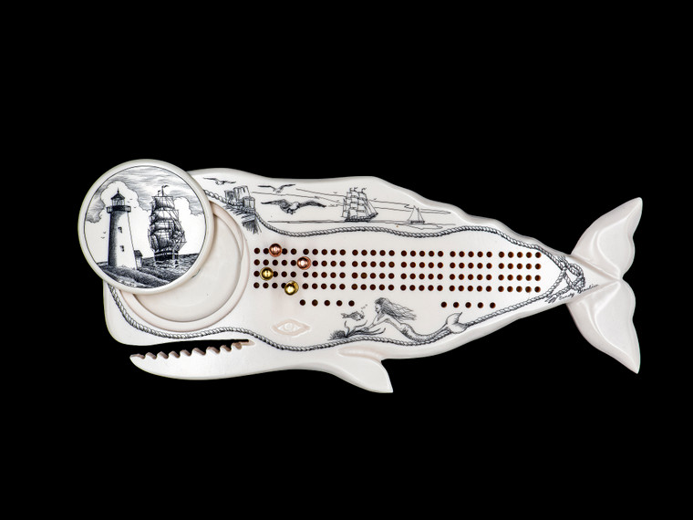 Whale Shaped Cribbage Board with Ship and Lighthouse piece with pegs showing.  This wonderful two person and our two team cribbage boards is a beautiful accent piece for your home or take it on the road for use as a travel cribbage board.  With the magnet holding the center piece and pegs in place it is a stunning travel cribbage board that will keep the pegs in place. 

This is a beautiful originally hand etched Ship and Lighthouse Eco - Ivory Scrimshaw Whale Shaped Cribbage Board!  The center circular piece has a magnet holding it in place.  Pushing on the base of the piece pops the Large round off the board, where the pegs are stored.  All cribbage boards come with 3 Silver and 3 Gold Metal pegs. 

The cribbage board itself is made for two players or teams.  The board has a native geometric design that was originally hand etched.  The large round piece has a magnet on the back to keep it secured to the board and store the pegs.  The pegs are made of wood.  This is part of the Save the Elephant Collection and was originally hand etched by Linda Layden.  The SKU is NC 53 - 406.

The Cribbage Board is 9.00" x 3.54" x 0.48".  It weighs 7.35 oz.