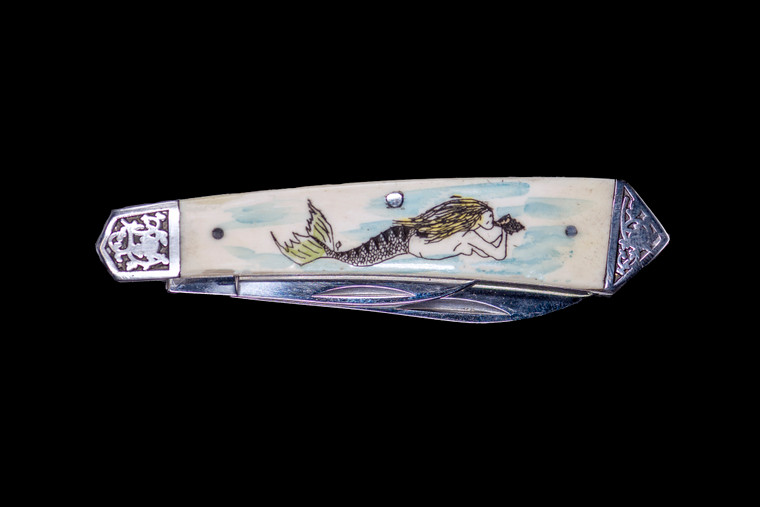 This stunning hand etched Colored Mermaid design on a 440 Stainless Steel Dual Blade Knife.  The knife design is similar to the Shrade 2222 knife.  This beautiful knife is part of the Scrimshaw Collection, with those words laser engraved into the blade.  The DB 2222 knifes come with the pictured leather sheath and each scale is made with Bovine Bone.  The DB 2222 knife has bolsters that are nickel silver with brass pins and liner.  It is a dual blade knife and a very useful pocket knife.  The dimensions of the DB 2222 Pocket Knife with the blade closed are 3.48" x 0.90" x 0.58".  The large blade itself is approximately 2.67" making the width of the knife with an open blades 6.15".  The small blades length is approximately 1.90".  The SKU is DB 2222 - 139C.


The scrimshaw is inked with colored india ink and sealed with renaissance wax, which is used by museums for antique restoration.  It also helps bring out the beauty of the artwork as well as in the cow bone. The knife is water resistant, but not waterproof.