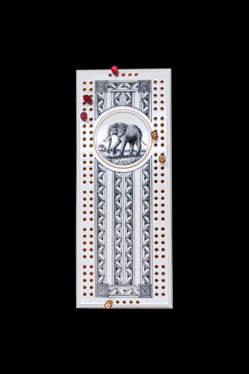 Elephant Cribbage Board with pegs.  This wonderful two person and our two team cribbage boards is a beautiful accent piece for your home or take it on the road for use as a travel cribbage board.  With the magnet holding the center piece and pegs in place it is a stunning travel cribbage board. 

This is a beautiful originally hand etched Elephant Design Eco - Ivory Scrimshaw Cribbage Board!  The center circular piece has a magnet holding it in place.  Pushing on the base of the piece pops the Large round off the board, where the pegs are stored.  All cribbage boards come with 3 red and 3 white/yellow wooden pegs. 

The cribbage board itself is made for two players or teams.  The board has a native geometric design that was originally hand etched.  The large round piece has a magnet on the back to keep it secured to the board and store the pegs.  The pegs are made of wood.  This is part of the Save the Elephant Collection and was originally hand etched by Linda Layden.  The SKU is NC 53 - 138.
