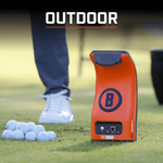 An orange Bushnell golf launch monitor sits on grass next to a pile of golf balls. A person's white shoe is visible behind it. Text overlay reads "OUTDOOR."