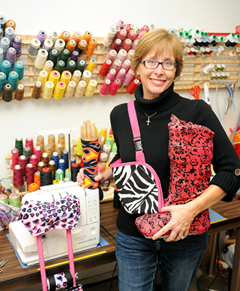 Annette De Lancey, founder of Cast Coverz! in a room full of sewing equipment, holding a boot cover, sling and crutch accessories 