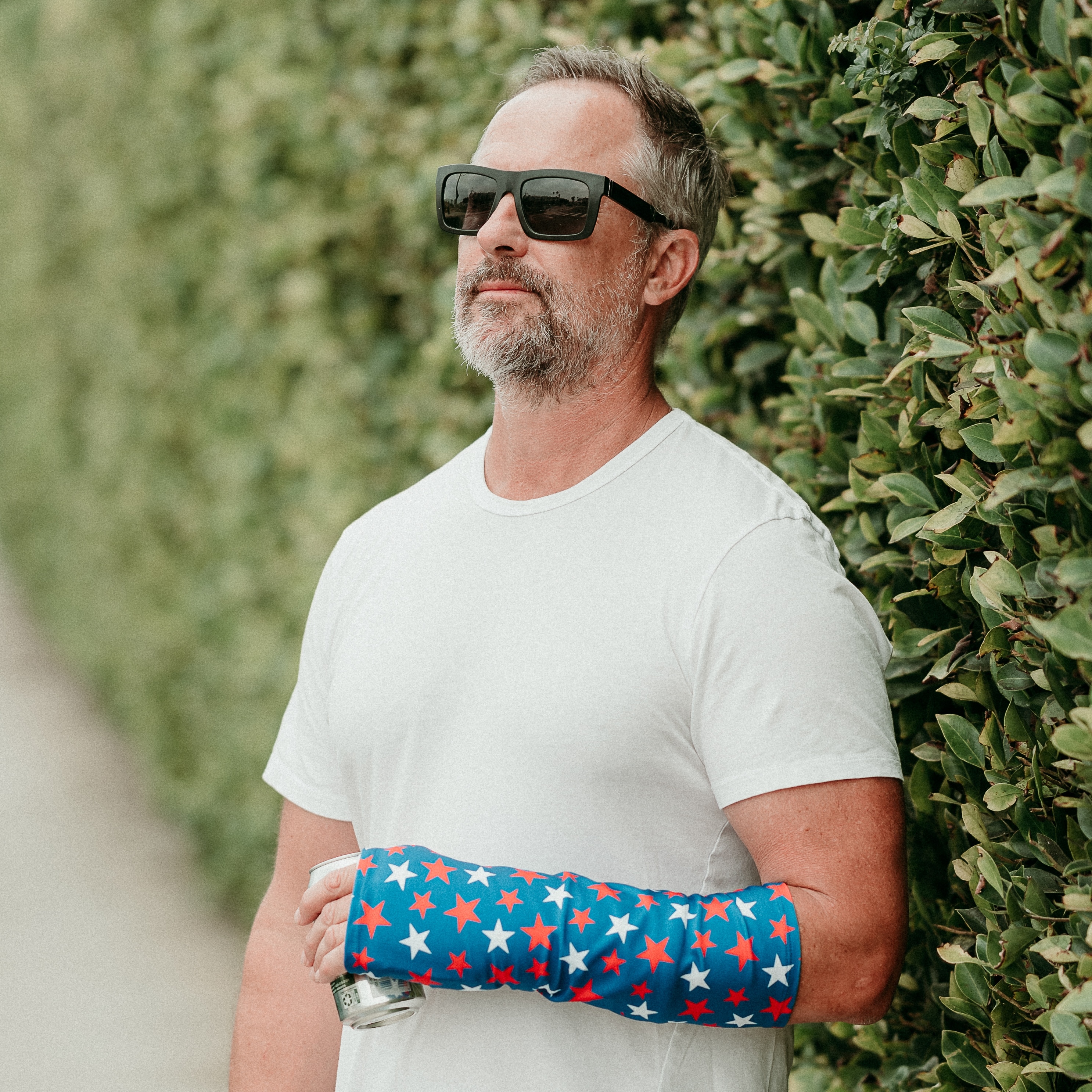 Man outdoors wearing a patriotic red, white, and blue arm cast cover during orthopedic recovery.