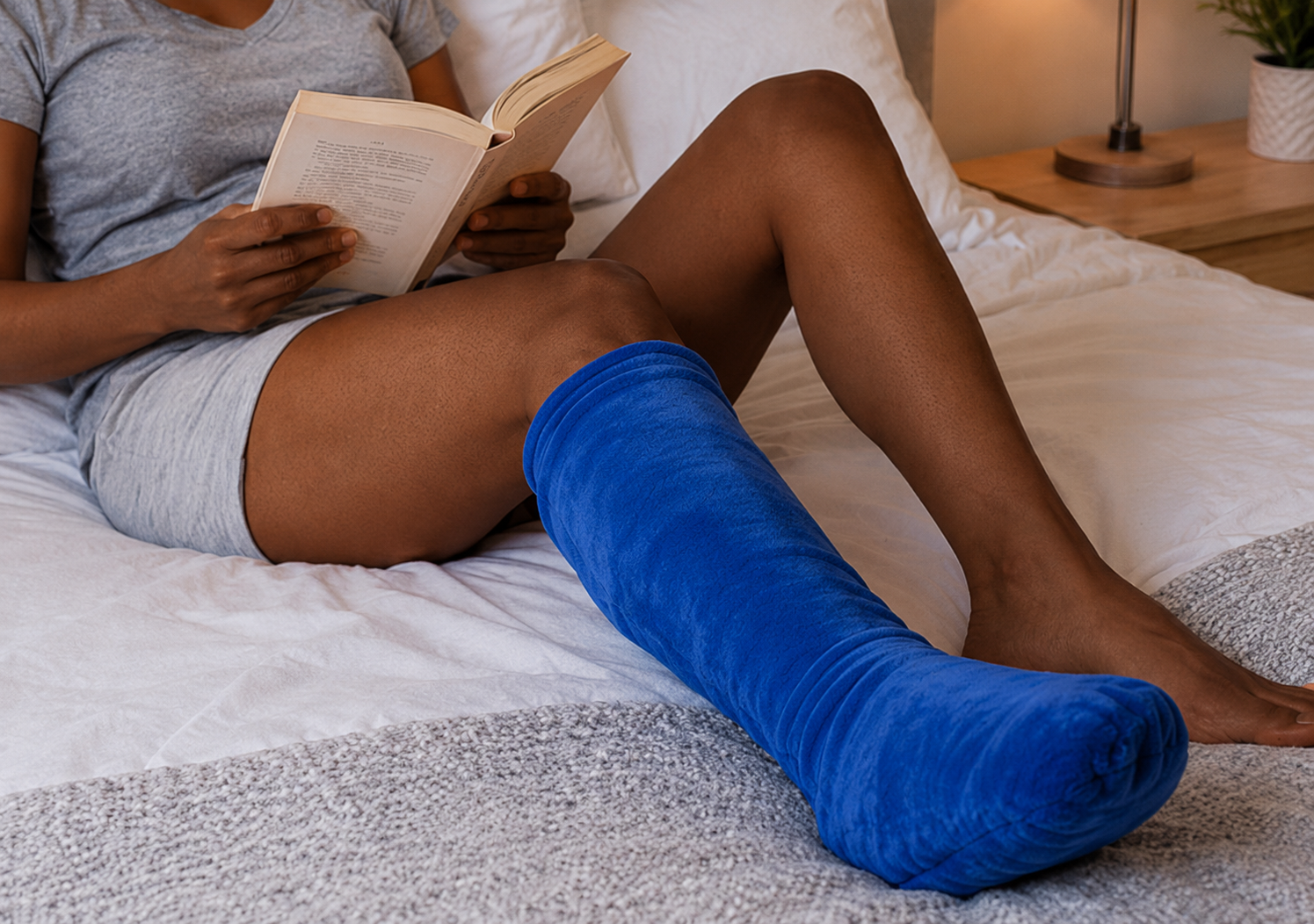 Woman resting in bed with an elevated leg cast covered by a soft cast cover for added comfort and bedding protection during recovery.