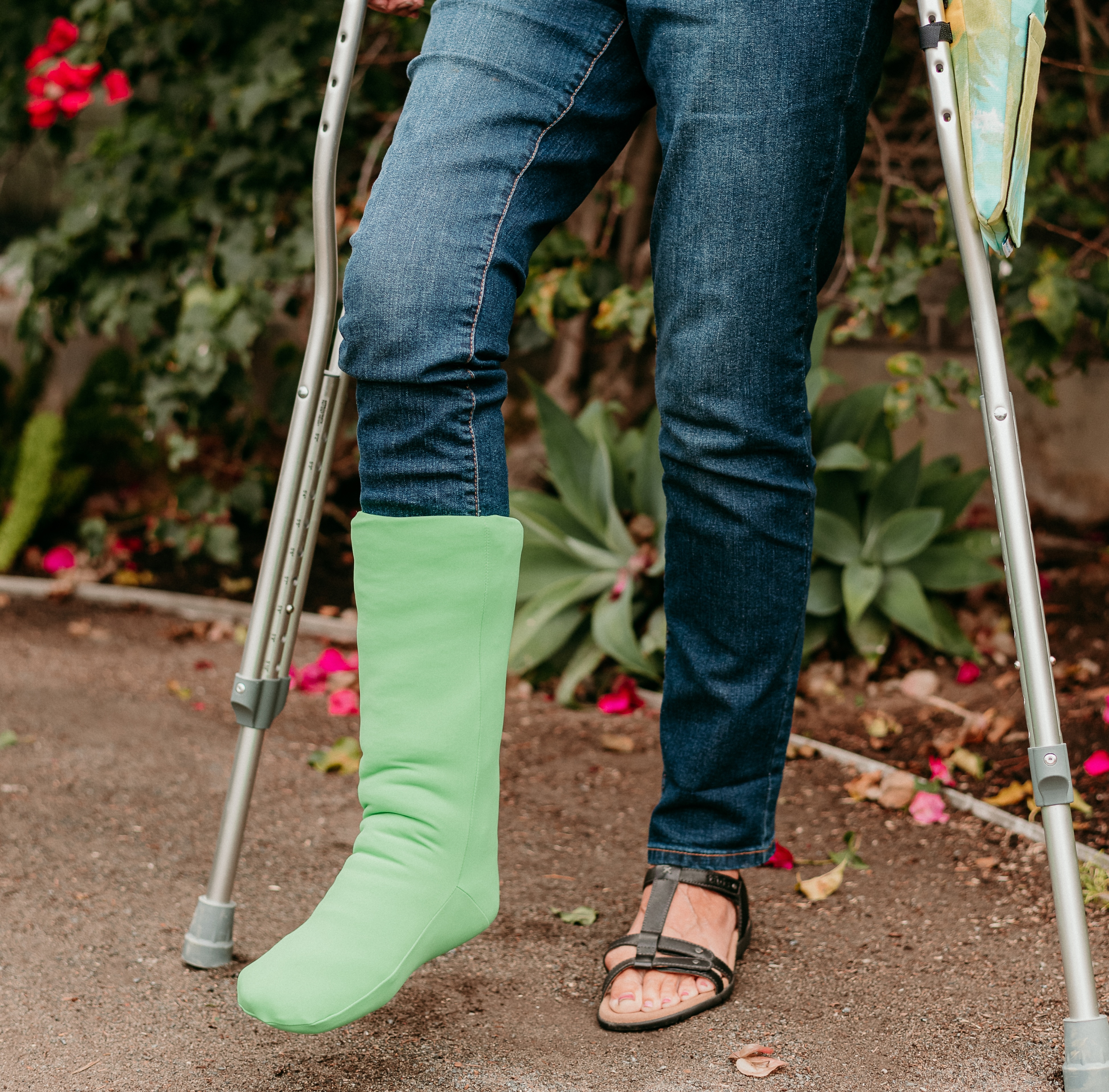 woman outside using crutches and wearing a green cover over a cast for a broken leg also has crutches and a matching crutch bag cover
