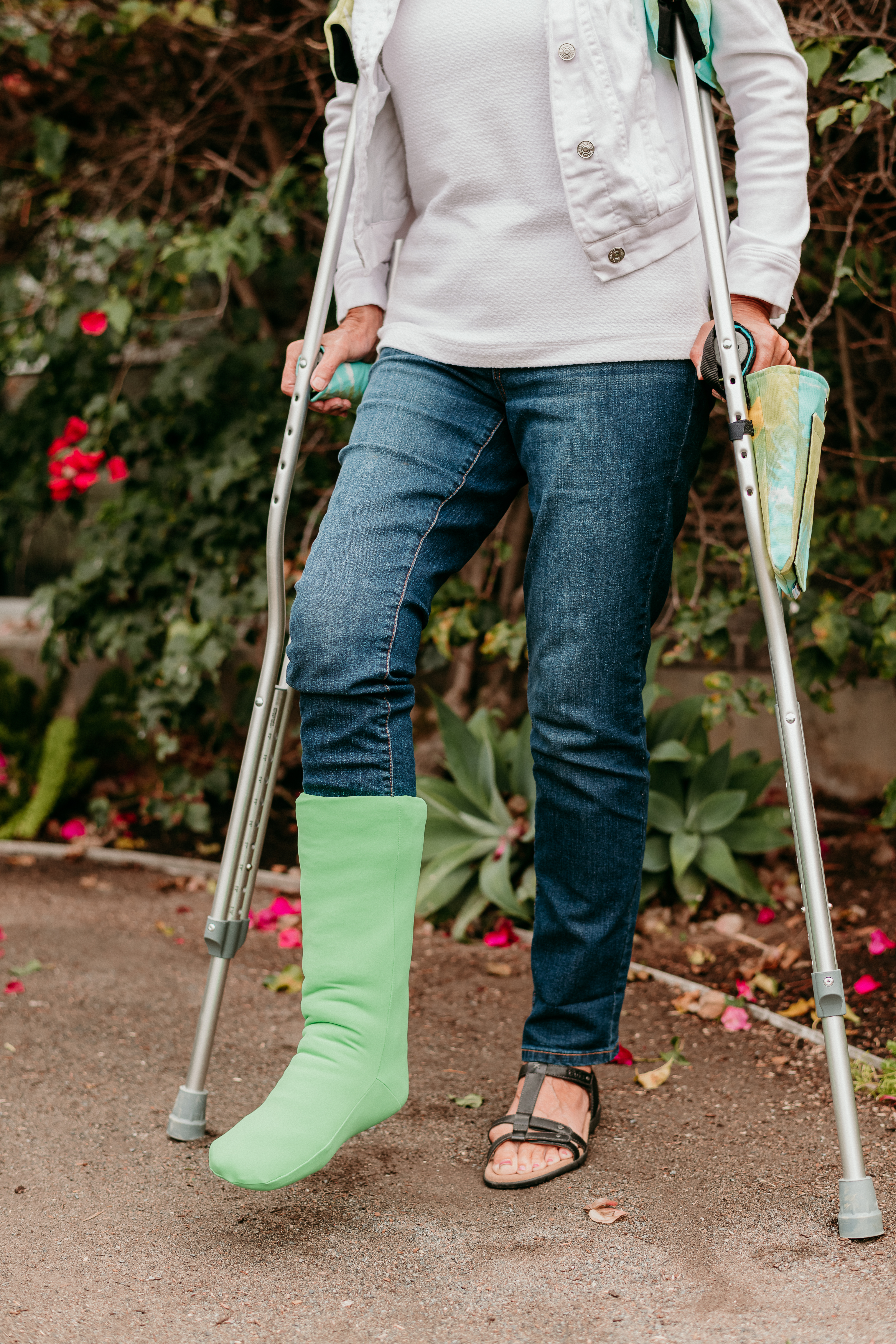 woman wearing a green cast cover over a broken leg standing outside also wearing crutches with green crutch covers 