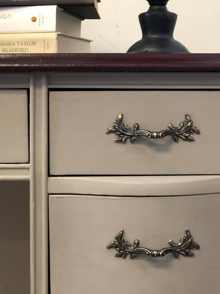 A white wooden desk with elaborate nickel finished pulls.