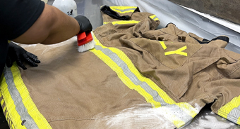 Firefighter turnout coat being scrubbed clean on a sterile table using a brush for proper PPE maintenance.