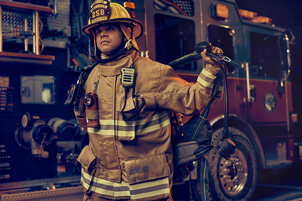 Firefighter in Globe turnout gear donning a MSA G1 SCBA in front of a fire truck.