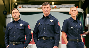 Three firefighters (two male, one female) standing in front of a fire truck in their navy blue uniforms