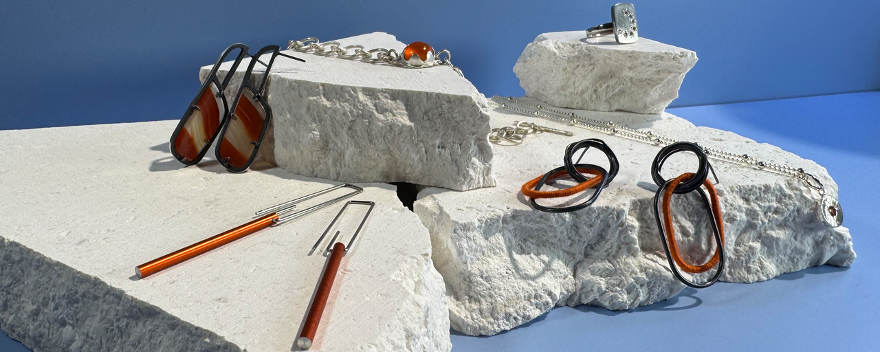 orange toned jewellery laying atop a white rock plinth with a powder blue background. 