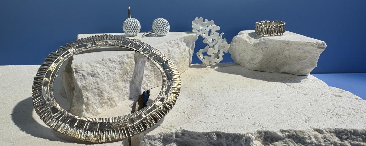 white coloured textured contemporary and a large silver bangle sit atop a tectured white stone against a blue background. 