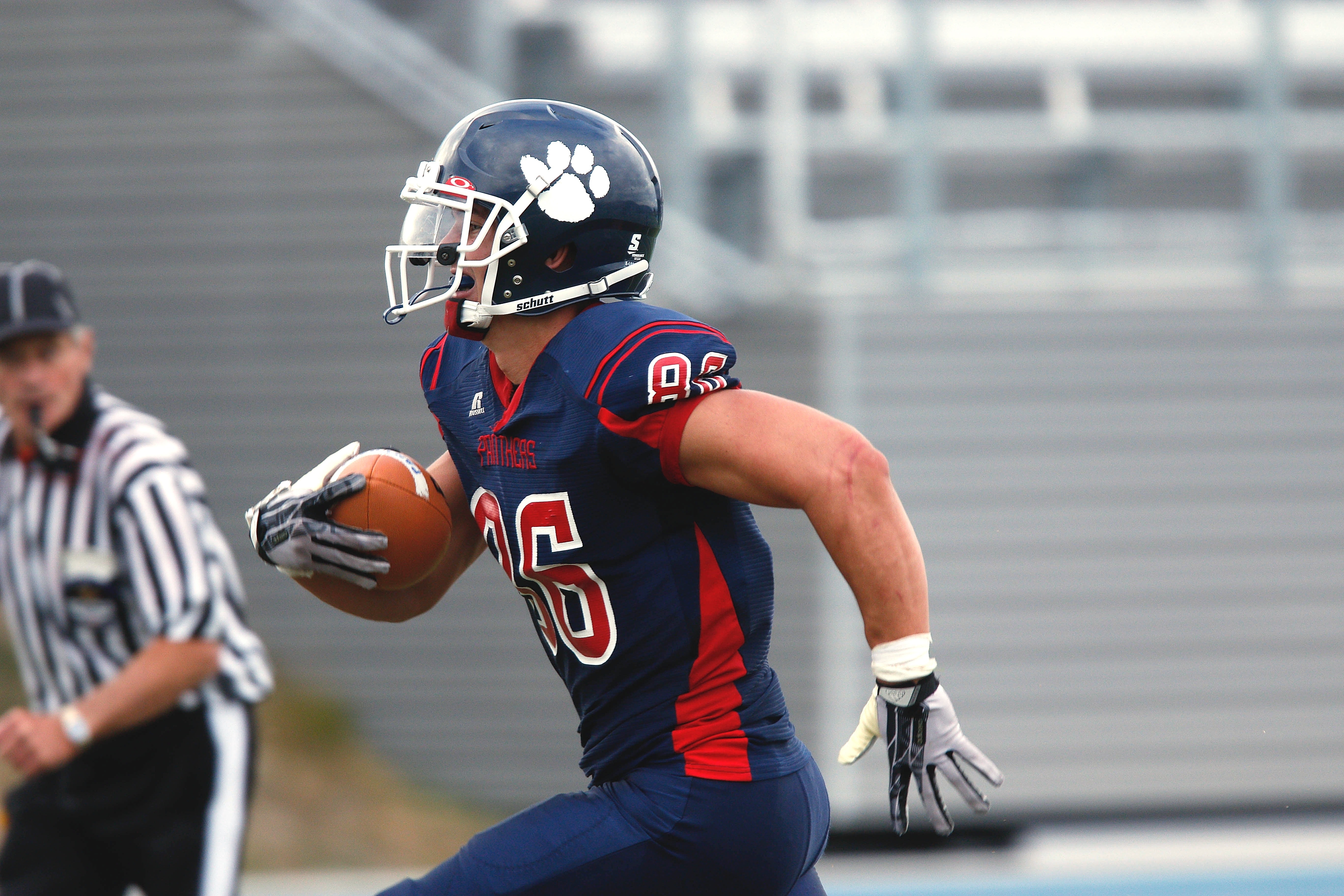 A football player running and a sports official blowing a whistle