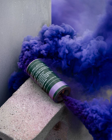 Purple smoke grenade resting on a concrete ledge, dense purple smoke pluming sideways against a wall