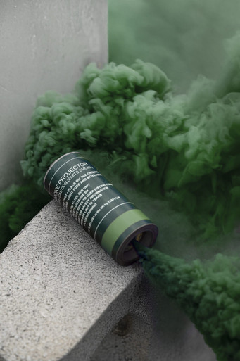 Green smoke grenade resting on a concrete ledge, green smoke curling upward against a wall corner