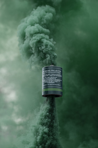 Green smoke grenade with a tall, dense green smoke column rising straight up against a blurred backdrop
