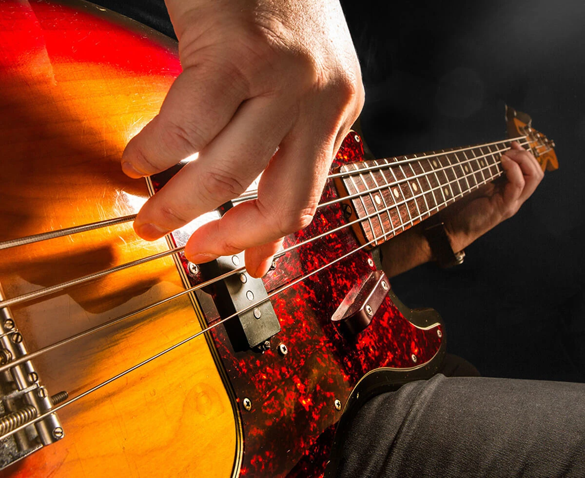 A player's hand plucking the strings of a four-string bass near the bridge.