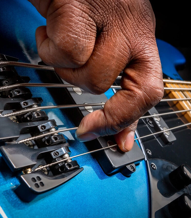 A player's hand plucking the strings of a five-string bass near the bridge.