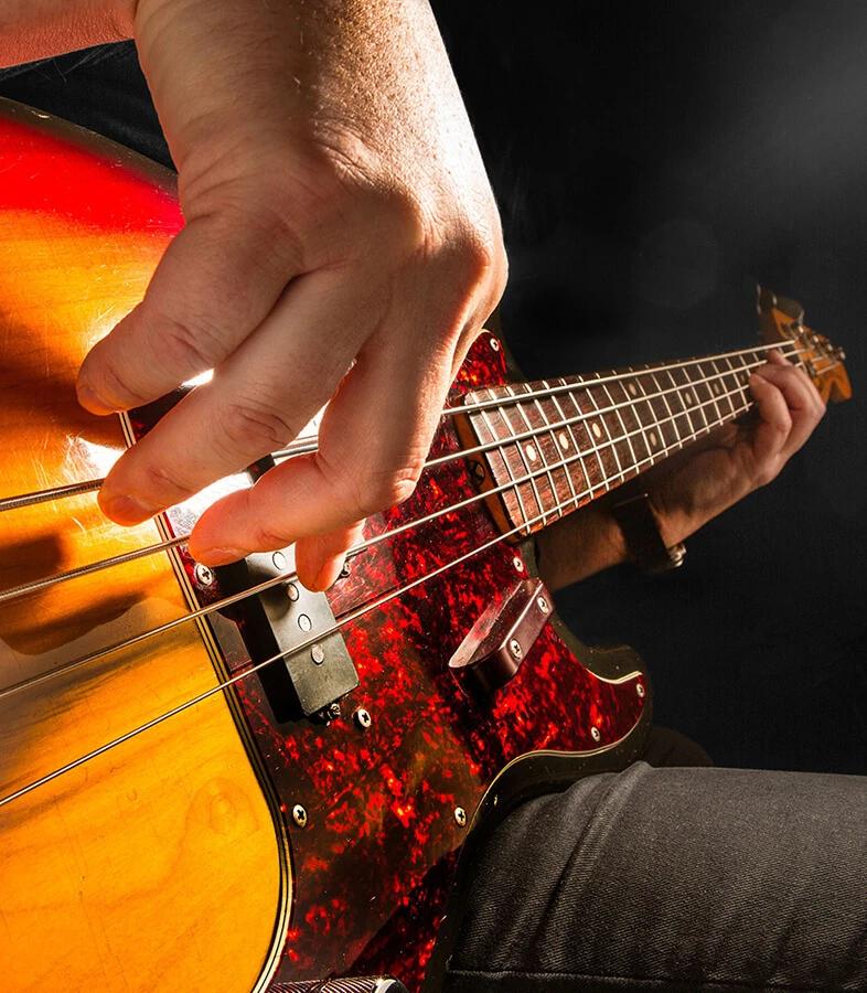 A player's hand plucking the strings of a four-string bass near the bridge.