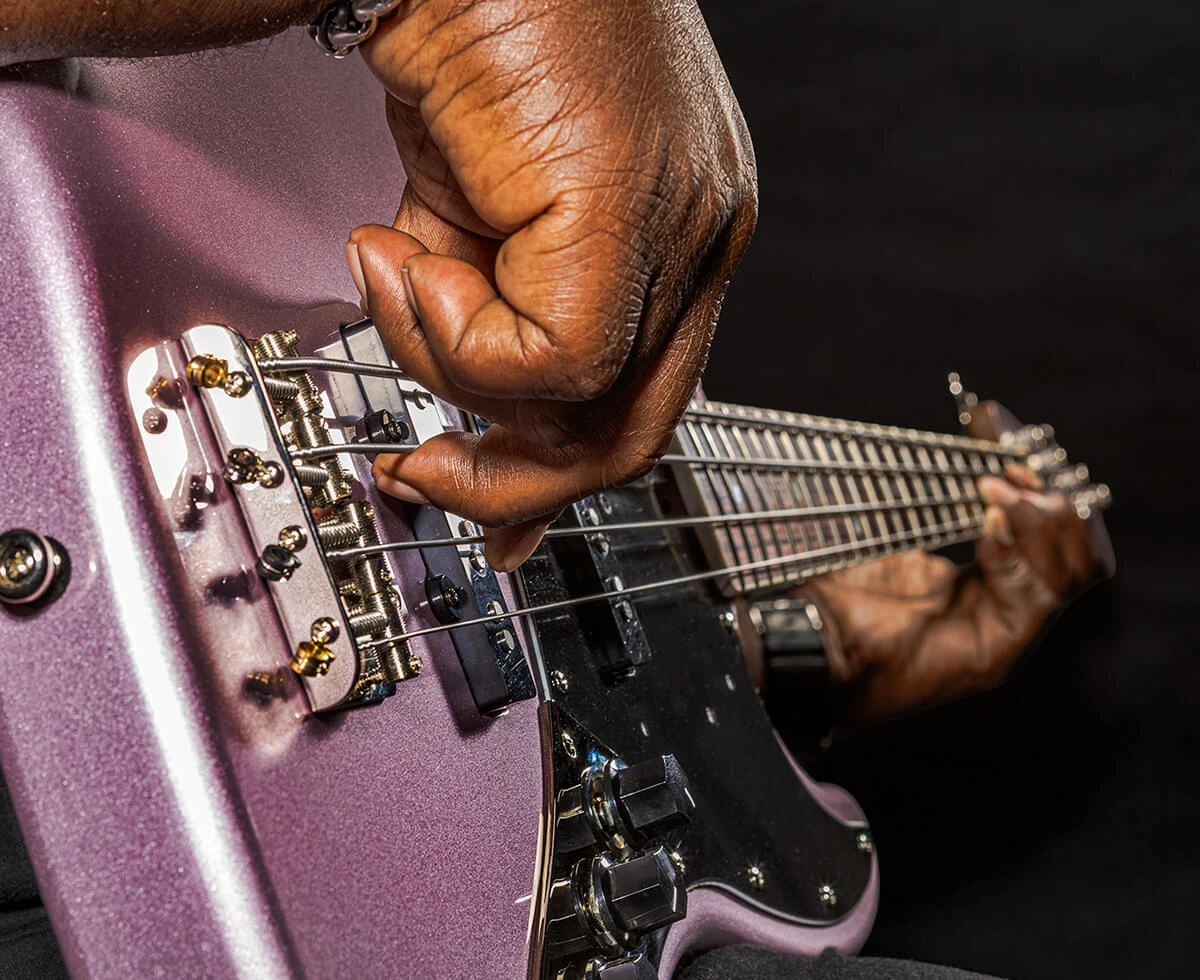 A player's hand plucking the strings of a four-string bass near the bridge.