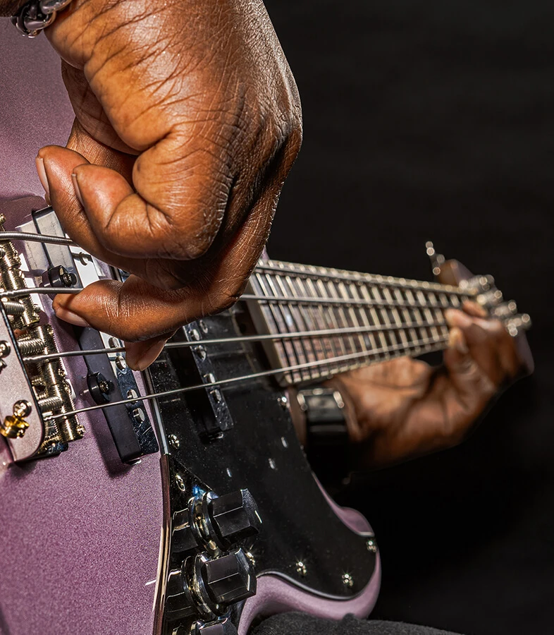 A player's hand plucking the strings of a four-string bass near the bridge.