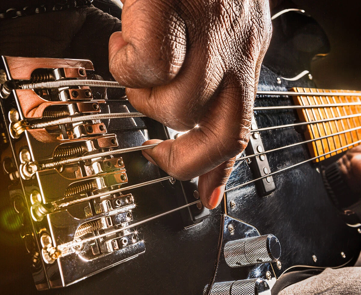 A player's hand plucking the strings of a five-string bass near the bridge.