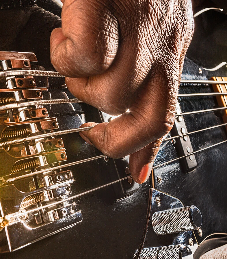 A player's hand plucking the strings of a five-string bass near the bridge.