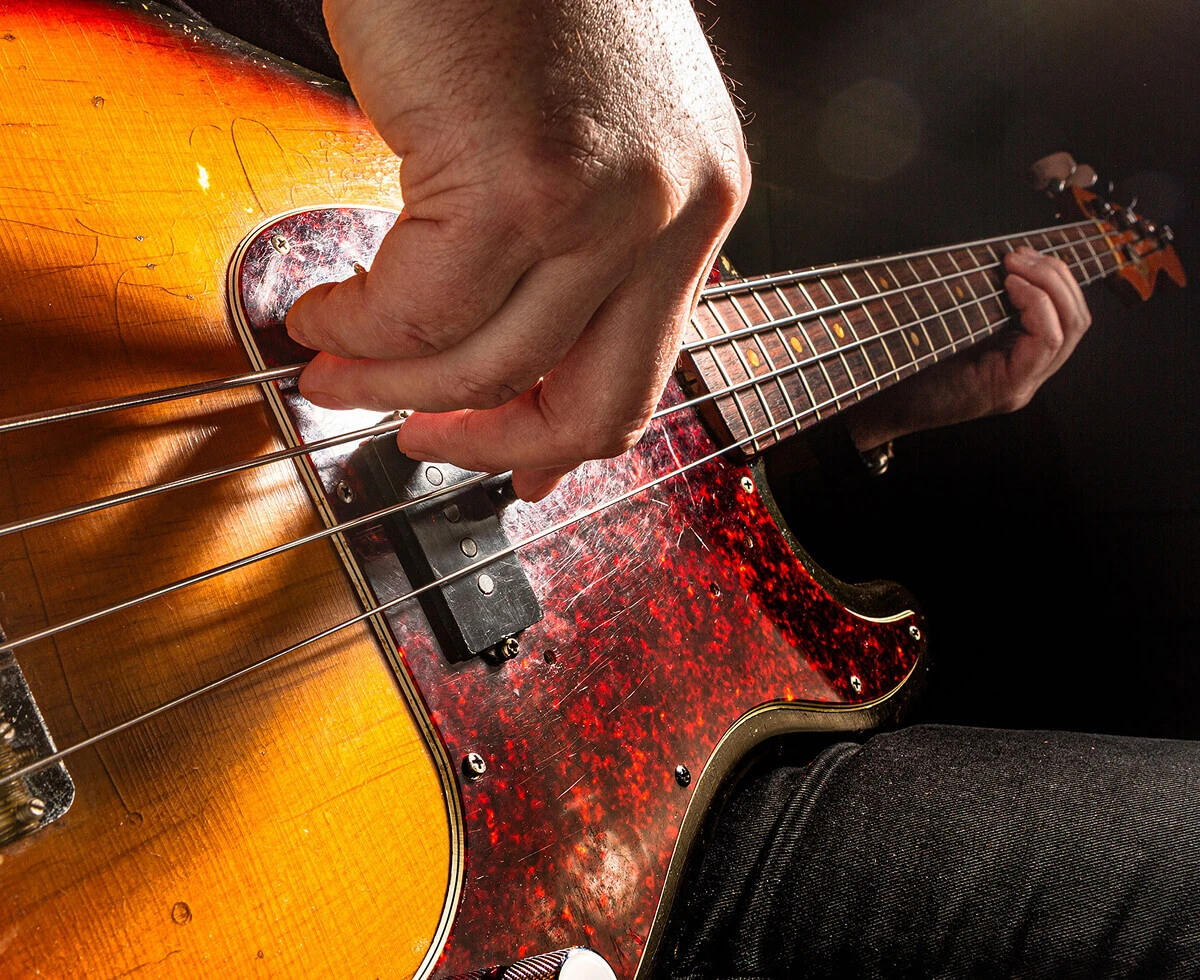 A player's hand plucking the strings of a four-string bass.