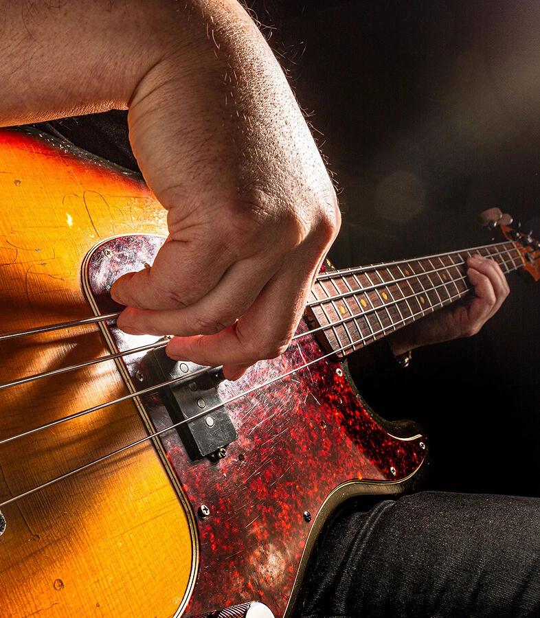 A player's hand plucking the strings of a four-string bass.