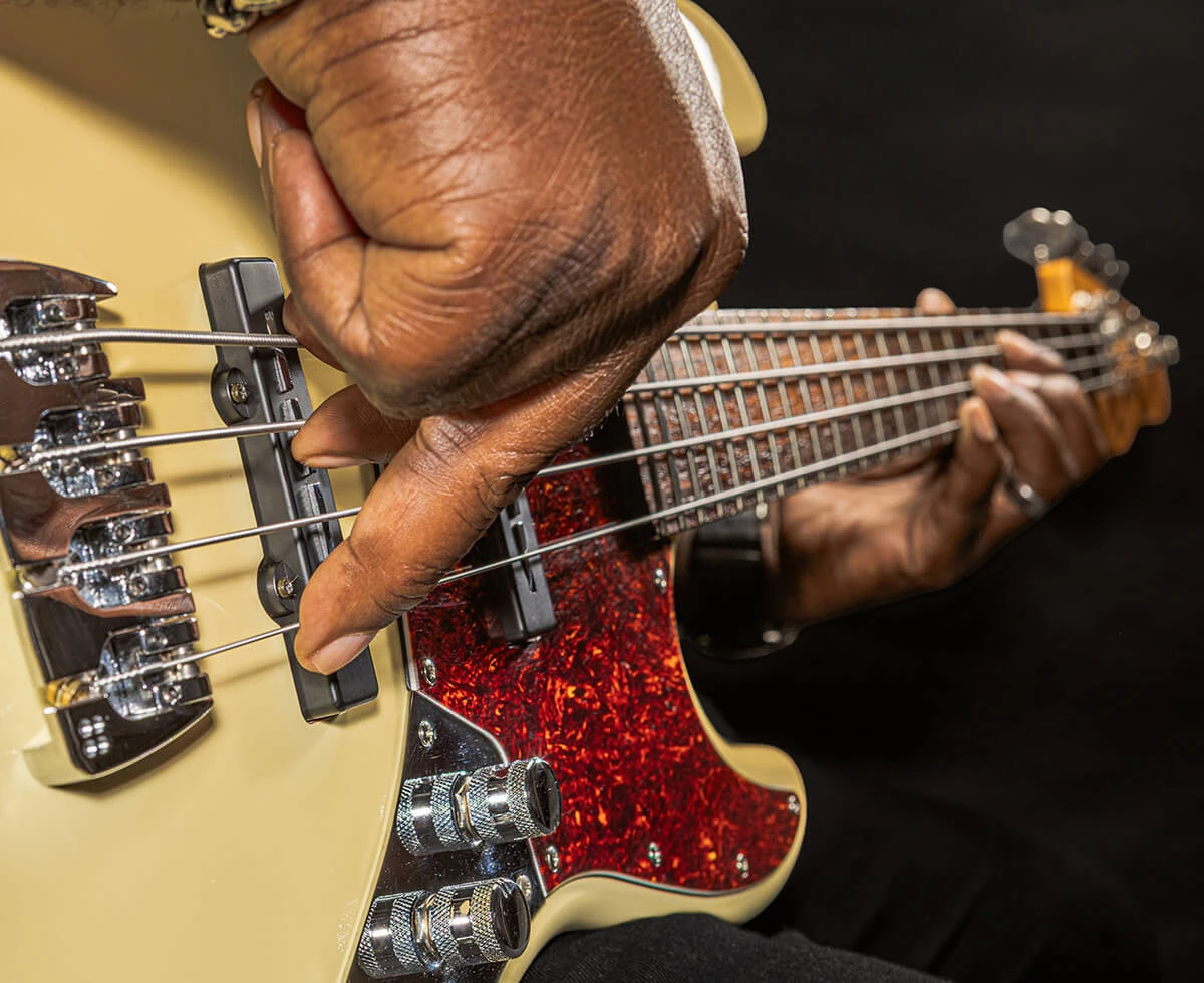 A player's hand plucking the strings of a four-string bass near the bridge.