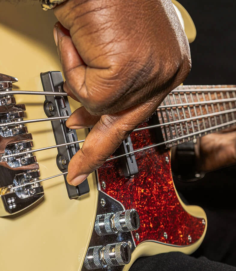 A player's hand plucking the strings of a four-string bass near the bridge.