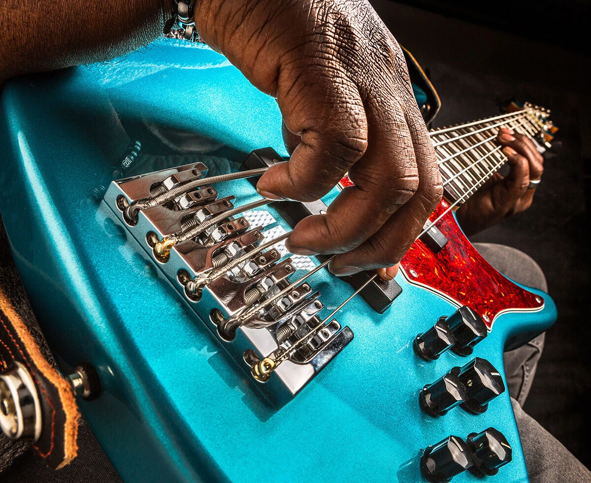 A player's hand plucking the strings of a five-string bass near the bridge.