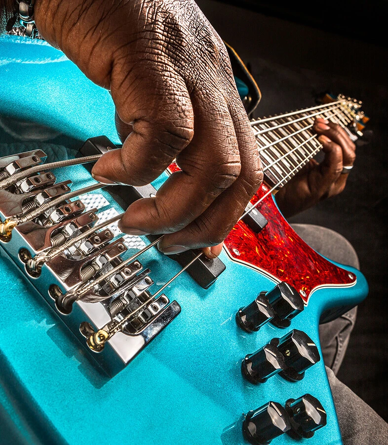 A player's hand plucking the strings of a five-string bass near the bridge.