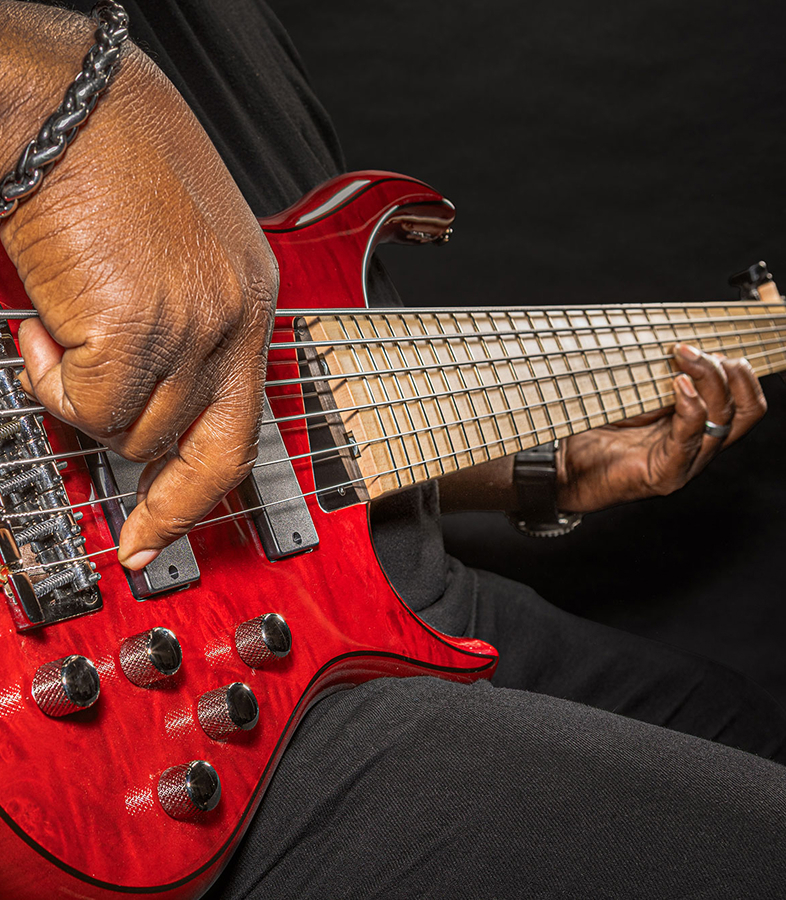  A player's hand plucking the strings of a six-string bass near the bridge.