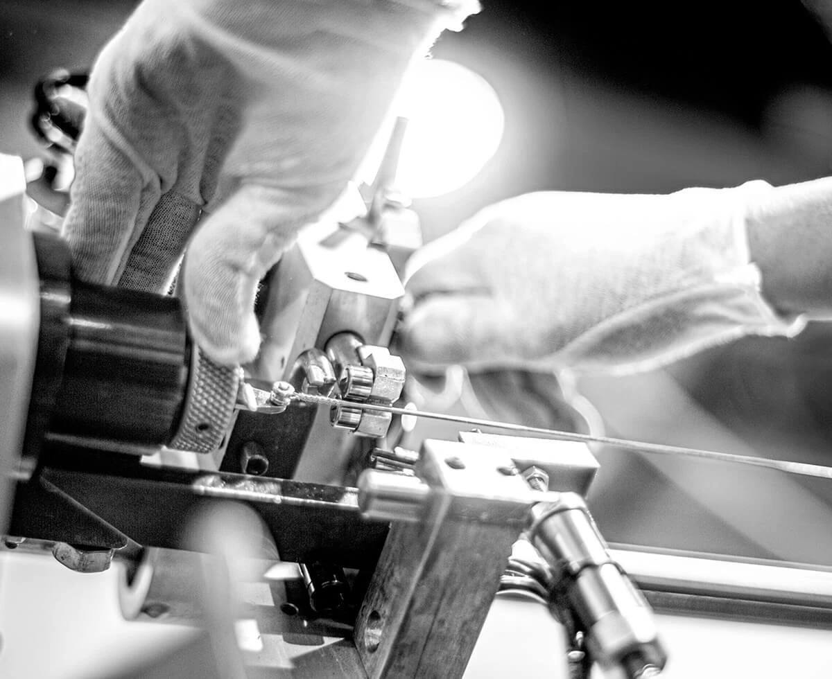 Gloved hands winding a bass string on a machine.