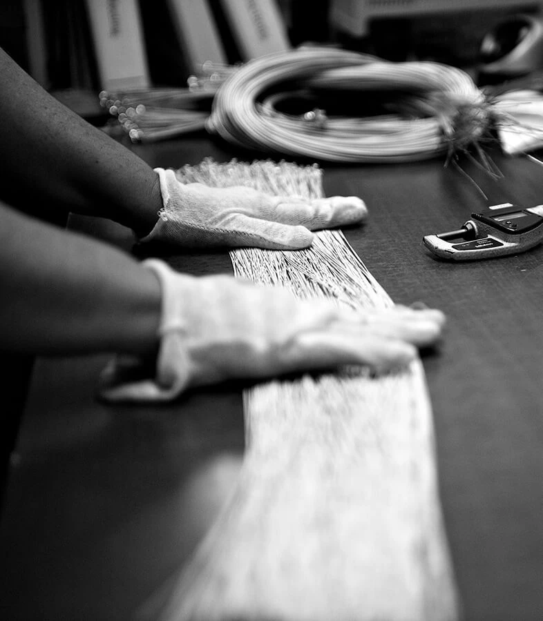 Gloved hands sorting bundles of bass string wire on a workbench.