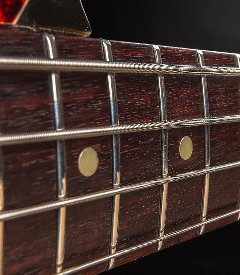 Bass strings running across the frets of a fingerboard.